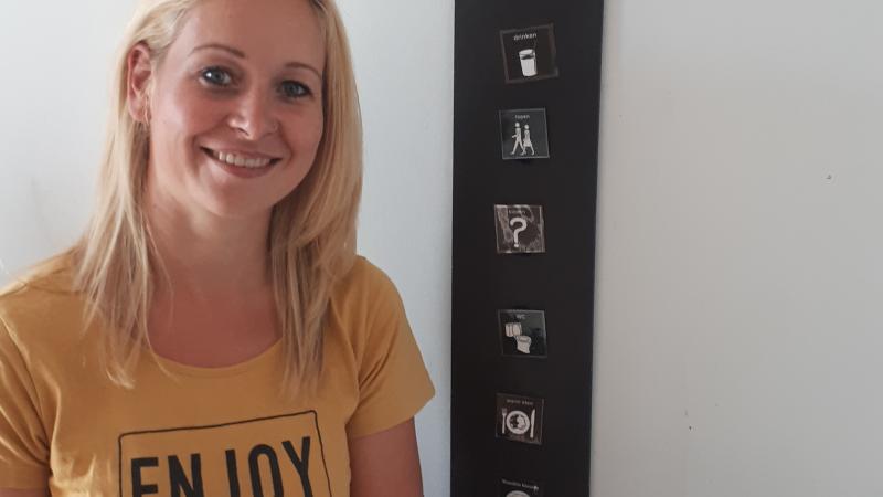 Begeleider Esther werkt bij een woongroep voor mensen met doofblindheid Begeleider Esther zit voor een bord met picto's